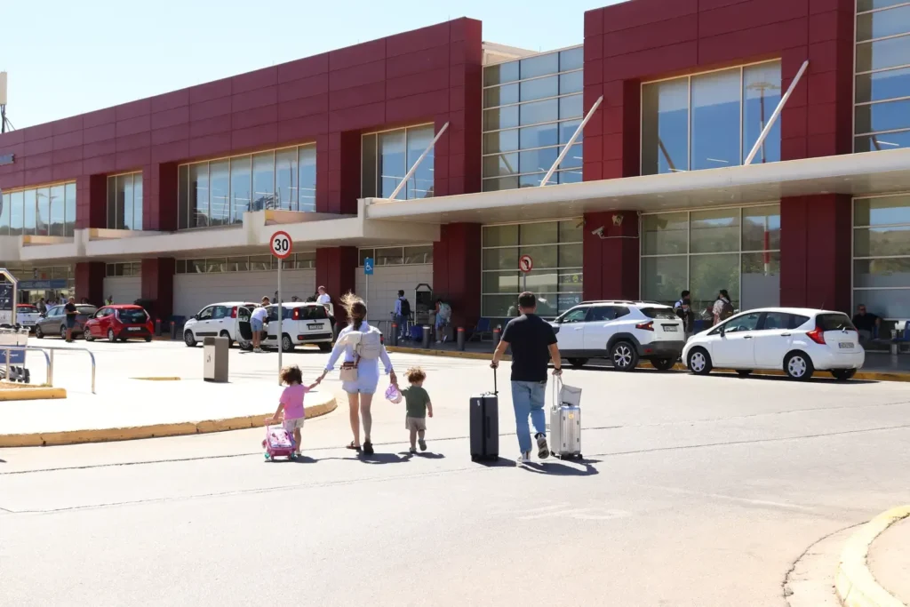 Family walking towards Chania International Airport (CHQ) terminal on a sunny day.