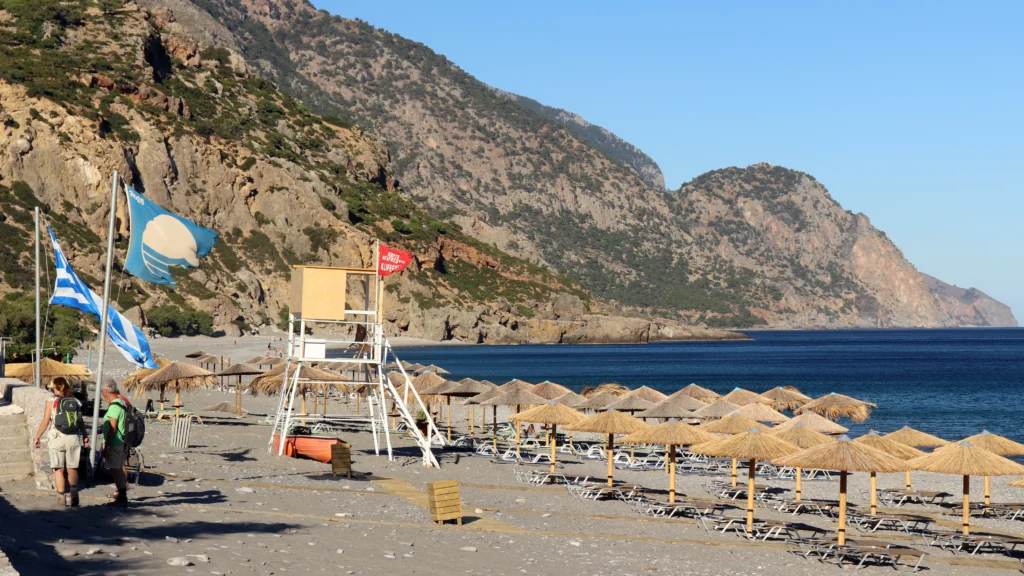 Panoramic view of Sougia Beach with sunbeds, Blue Flag, and the mountain backdrop on Crete's south coast