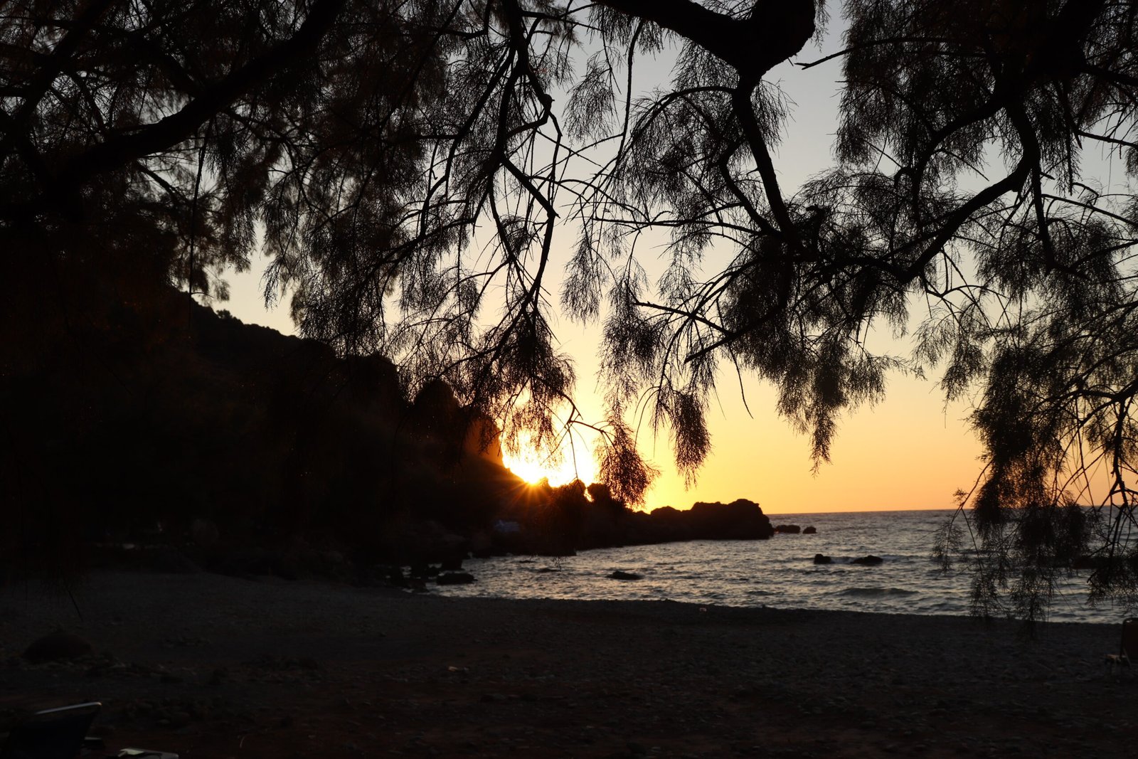 Sunset behind the rocks at Sfinari beach seen through tamarisk branches