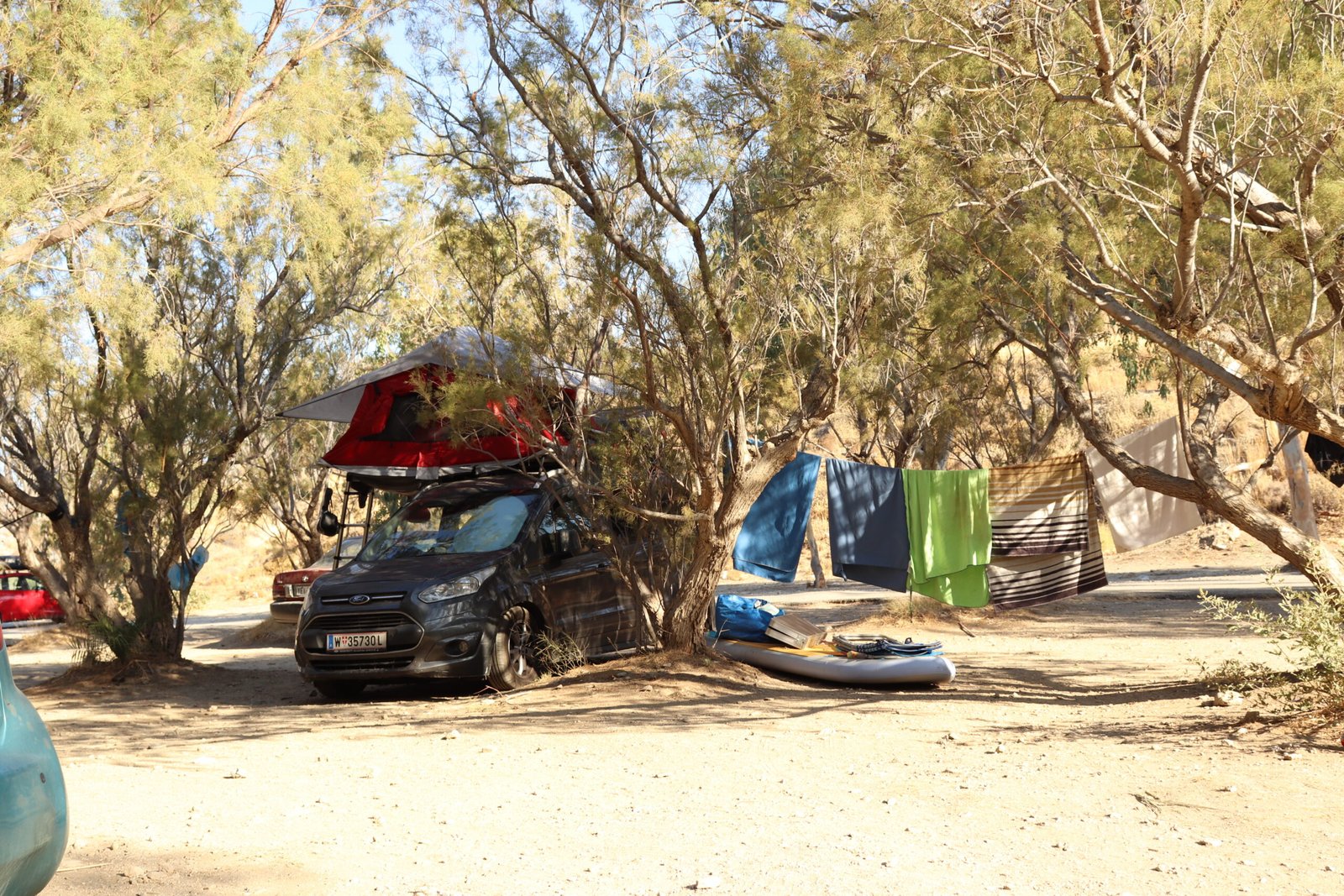 Camping spot under cypress trees at Ammoudi Beach near Plakias with parked camper and relaxed outdoor setup.