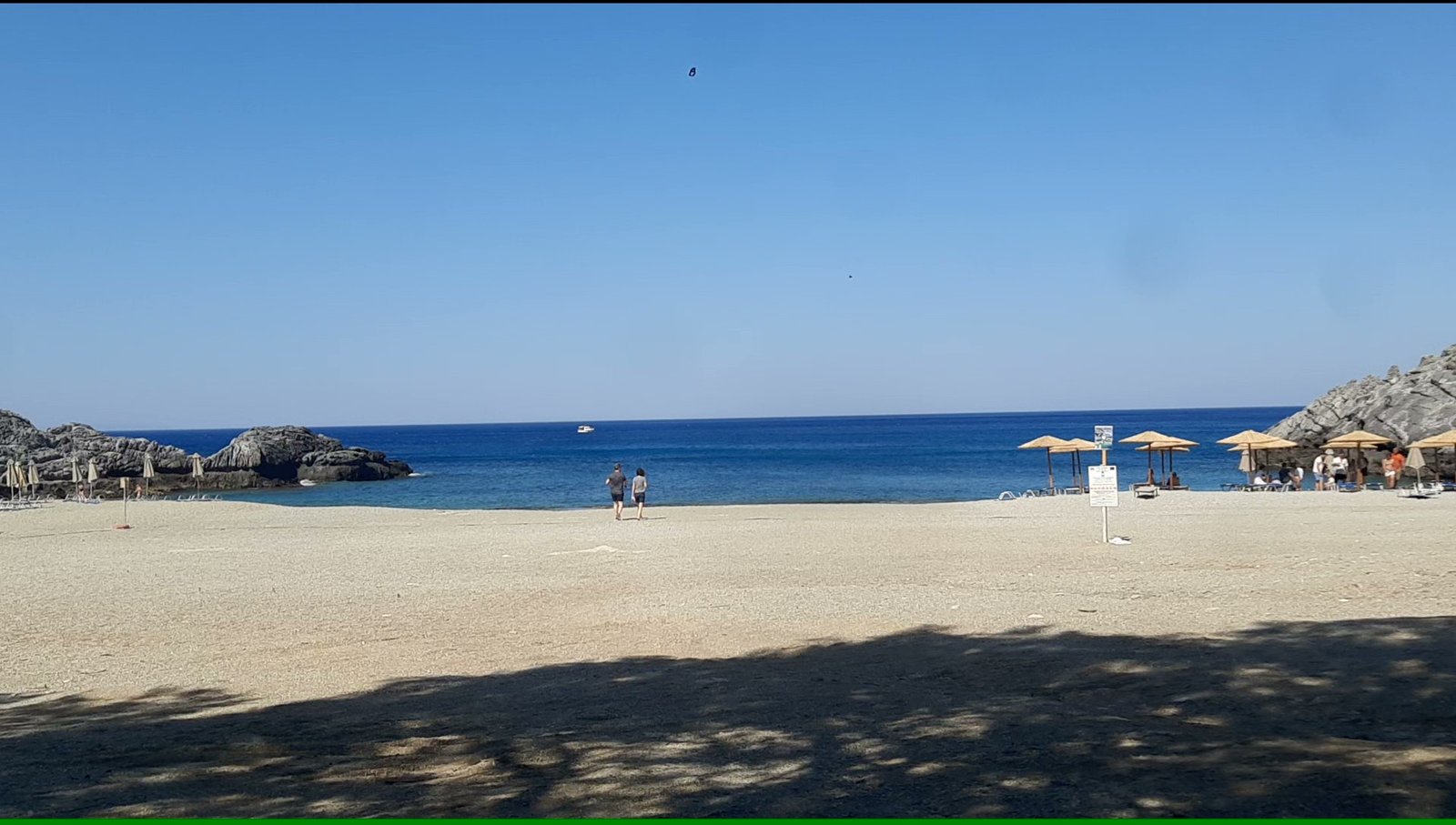 Wide sandy shoreline of Ammoudi Beach with umbrellas, calm water and rocky coves near Plakias, Crete.