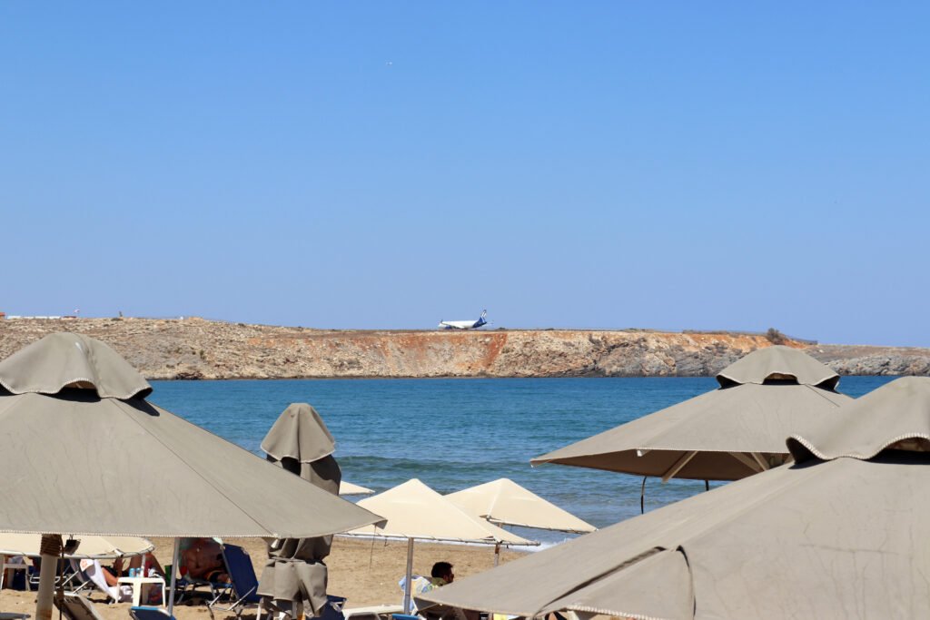 View of Karteros Beach with a plane landing at Heraklion Airport in the background